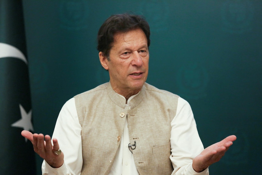 Pakistański premier Imran Khan macha ręką i umieszcza za sobą pakistańską flagę