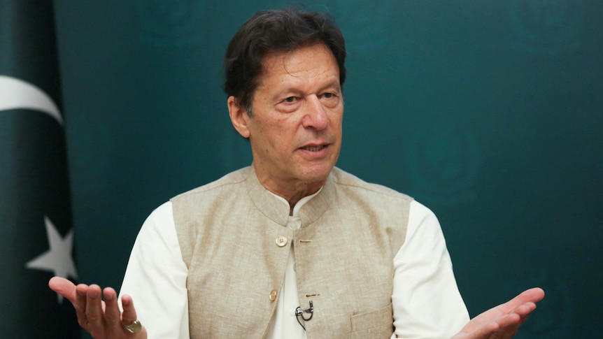 Pakistan's Prime Minister Imran Khan gestures with the palms of his hands, with a Pakistani flag behind him