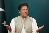 Pakistan's Prime Minister Imran Khan gestures with the palms of his hands, with a Pakistani flag behind him