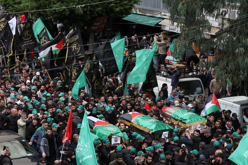 A large crowd carrying three caskets covered in Palestinian flags. 
