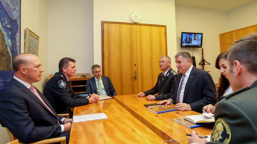 Peter Dutton, wearing suit, Andrew Colvin, wearing AFP uniform, sit at wooden table opposite men in suits in meeting room