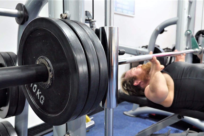 Man in black singlet does bench presses.