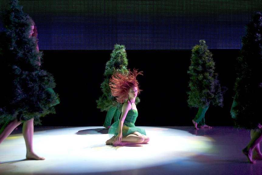 A woman in green on a stage lifts her red hair
