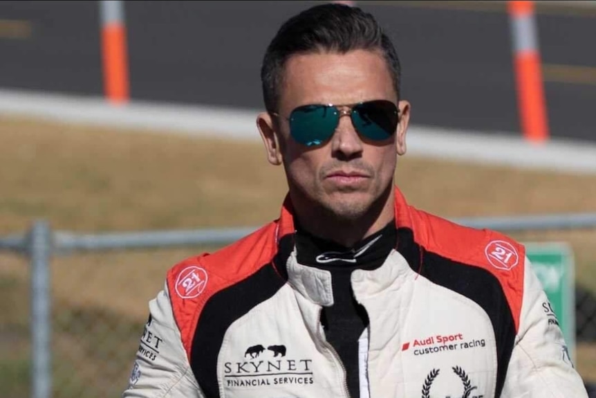A man wearing sunglasses and a racecar driver's outfit.