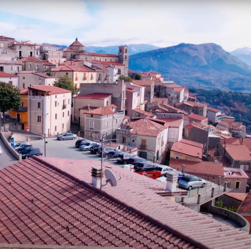 A row of houses sit on a cliff face under a blue sky.
