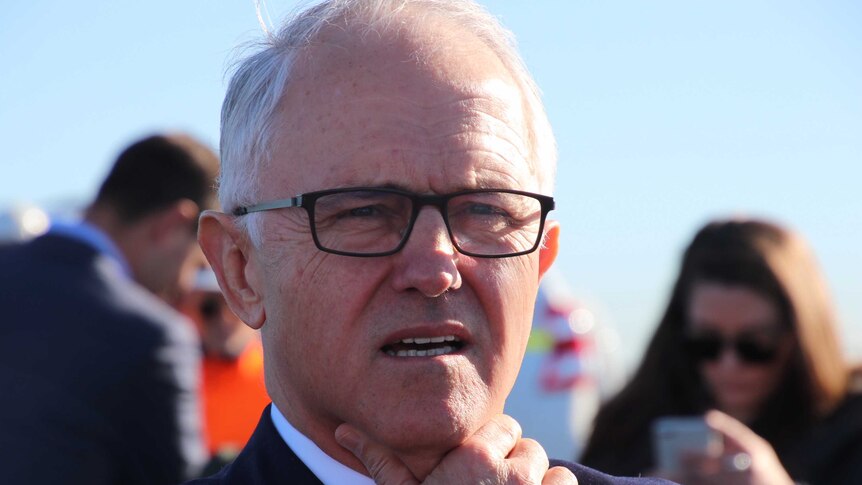 A head and shoulders shot of Prime Minister Malcolm Turnbull outdoors wearing glasses with his hand on his chin.