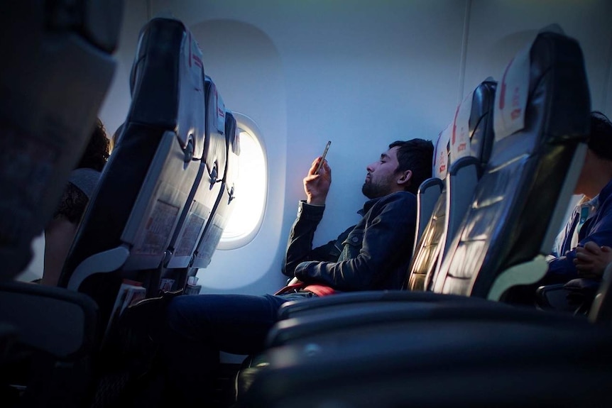 Man stares at his phone while on plane to depict travellers' tips for having a better flight.