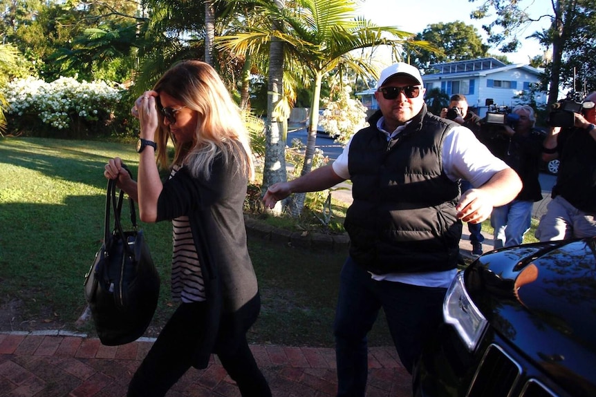 Mercedes Corby, clutching a handbag, walks along a driveway at Loganlea with a security guard following close behind.