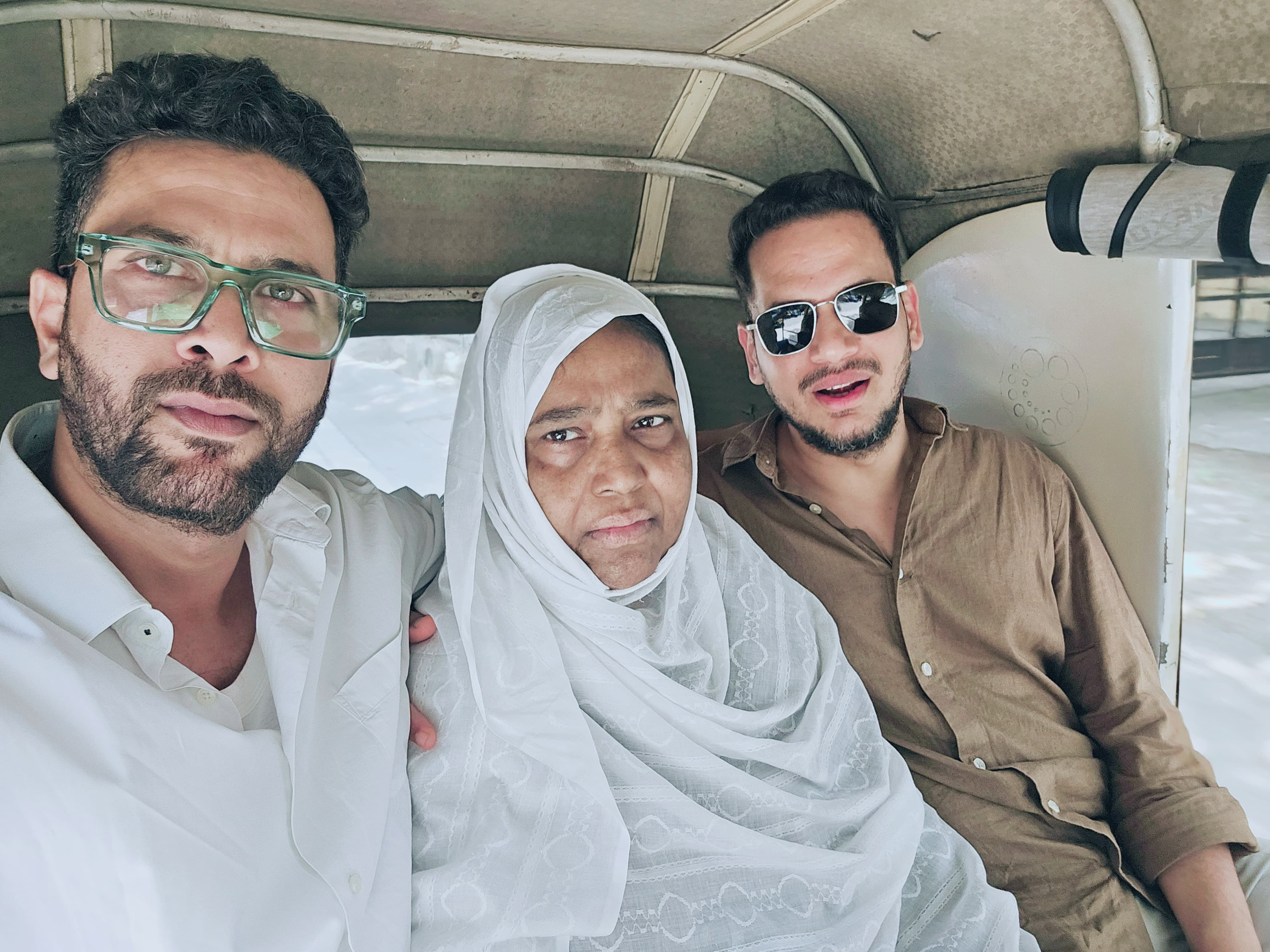 An older Indian woman in a hijab with her two sons on either side of her. 