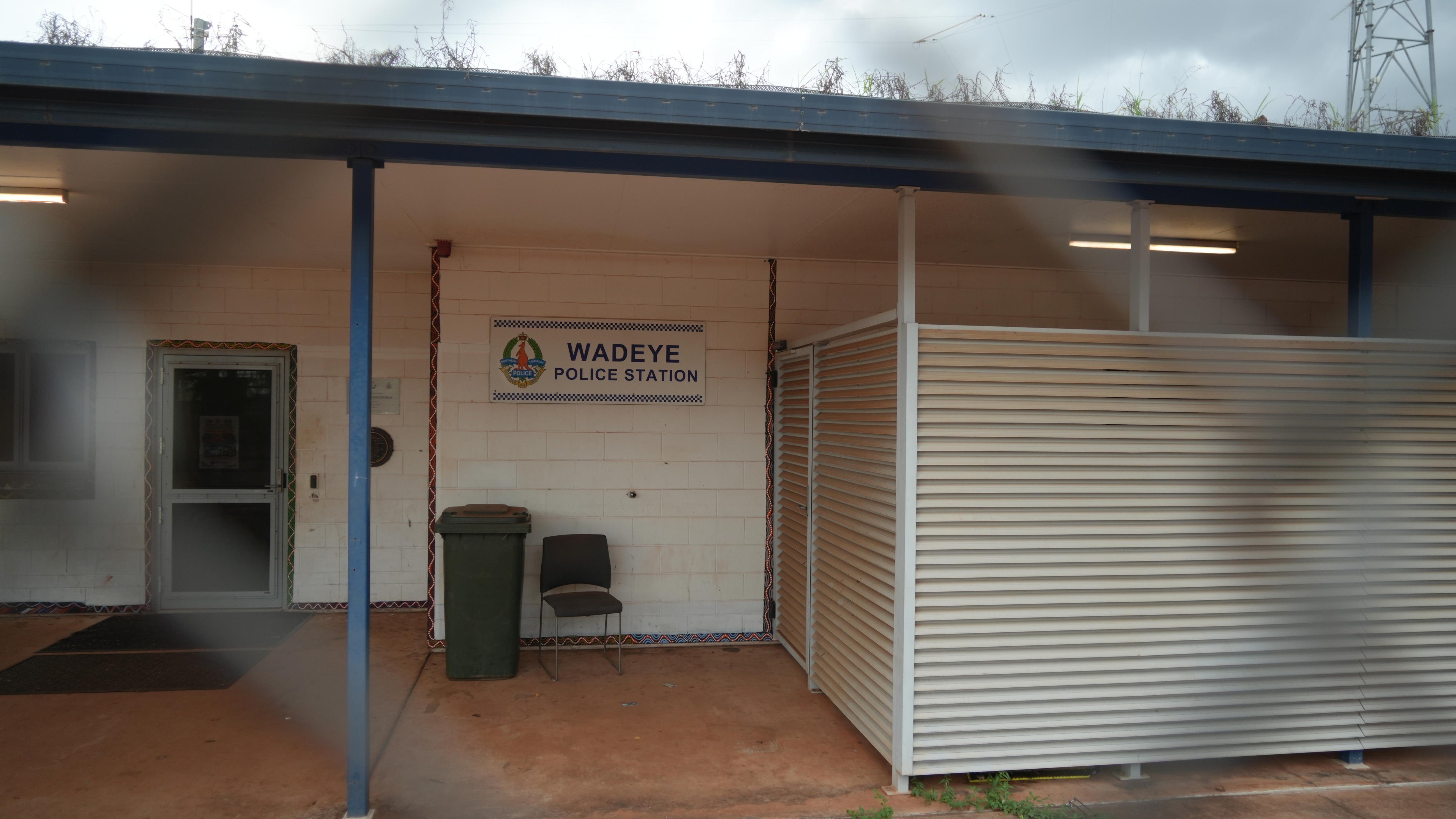 A sign on a white brick building reads "Wadeye police station" as seen through a cyclone fence.