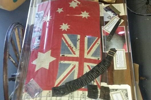 A Australian flag from 1901 and a leather bandolier in a glass case.