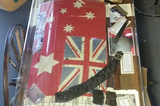 A Australian flag from 1901 and a leather bandolier in a glass case.
