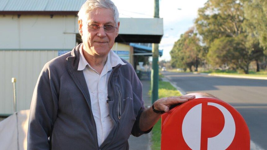 Yarloop post office licensee Ron Sackville stands next to a red post box on the side of the road.