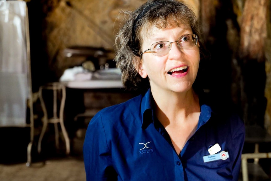 An image of a middle-aged woman with glasses and curly hair, inside a tunnel, looking up and out of the frame.