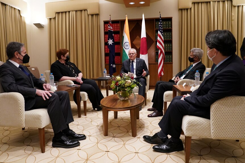 Cinq politiciens sont assis dans une réunion formelle, l'un sans masque facial alors qu'il s'adresse aux autres qui sont assis sur de grandes chaises