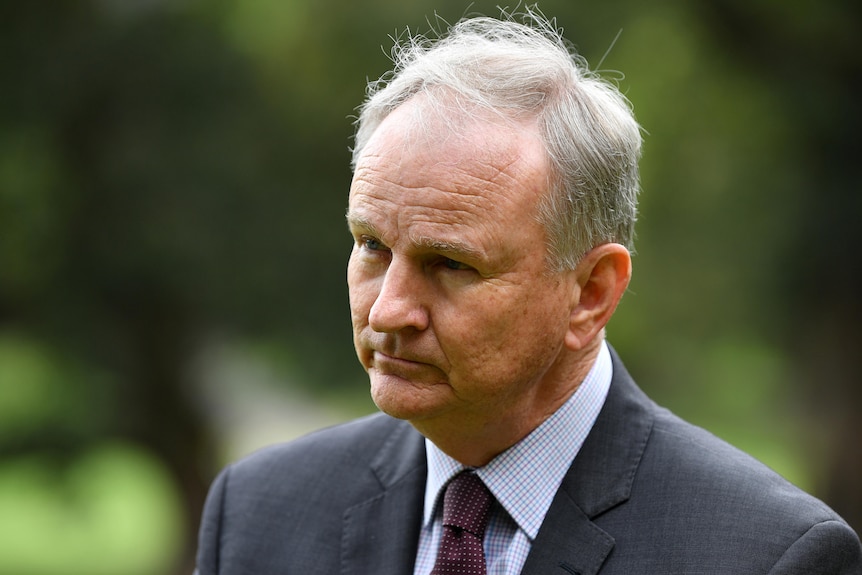 A close-up shot of a man in a suit and tie looking off-camera with a serious expression on his face. 