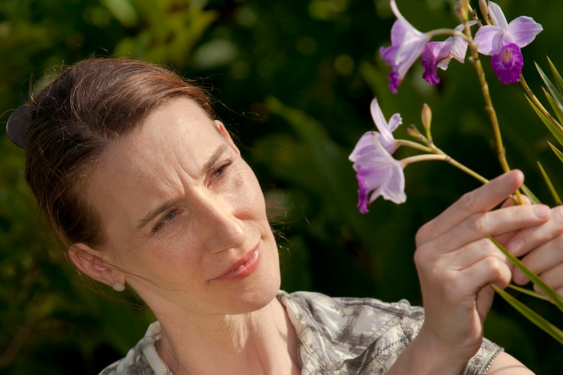 A woman looks at a purple orchid.