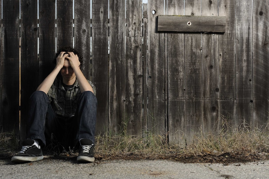 Depressed Teenager sits against a old wooden fence