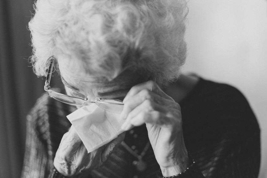 An old woman wipes her eyes with a handkerchief