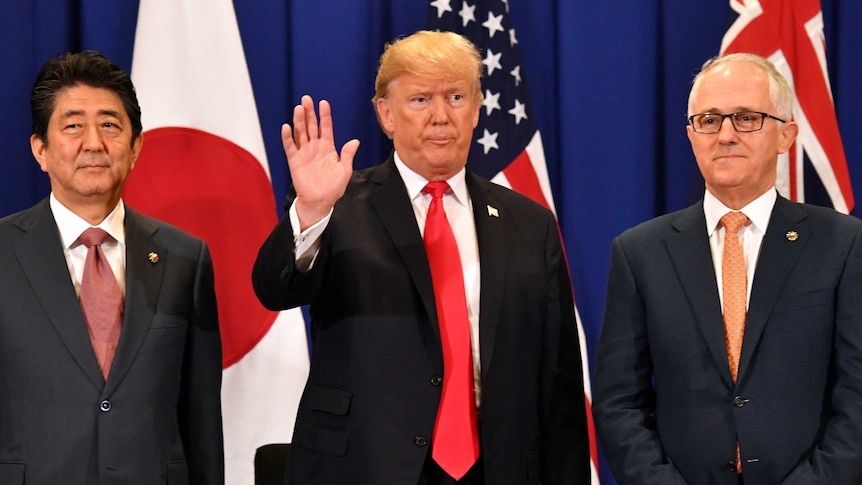 Shinzo Abe glances sideways while Donald Trump waves and Malcolm Turnbull looks dead ahead.