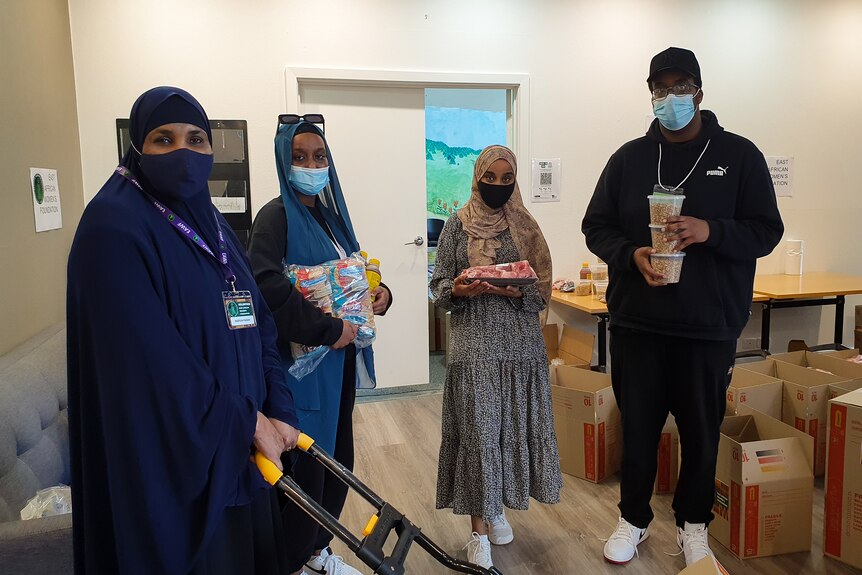 Three women in hijab and face masks and a man stand with cartons. 