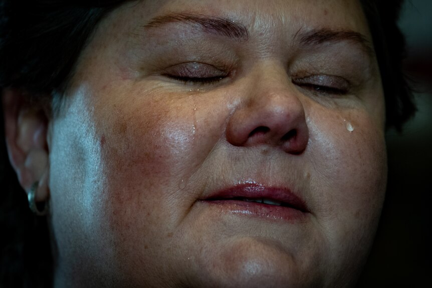 A close up of Heidi Arntzen's face shows her with eyes closed and a tear rollikng down her cheek.
