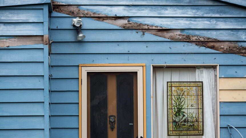 A blue housefront is marred with an unpainted line where a deck was once attached.