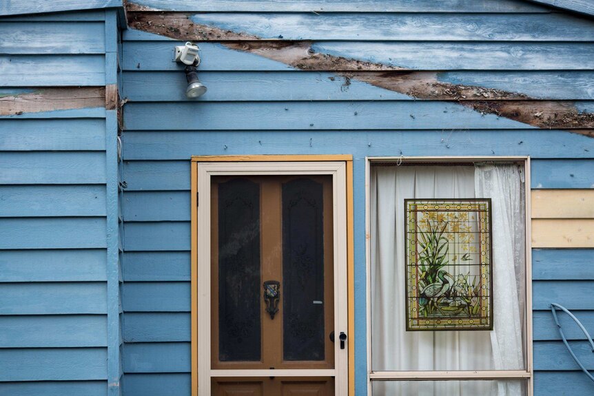 A blue house front is marred with an unpainted line where a deck was once attached.
