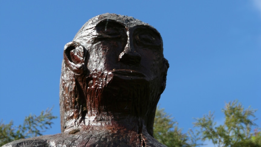 A wooden statue of a yowie against a blue sky.