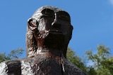 A wooden statue of a yowie against a blue sky.