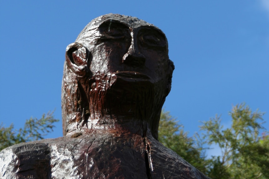 A wooden statue of a yowie against a blue sky.