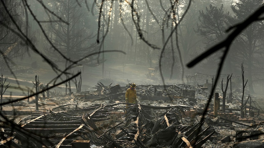 A firefighter works through the collapsed frames and charred wreckage of a trailer home destroyed by fire.