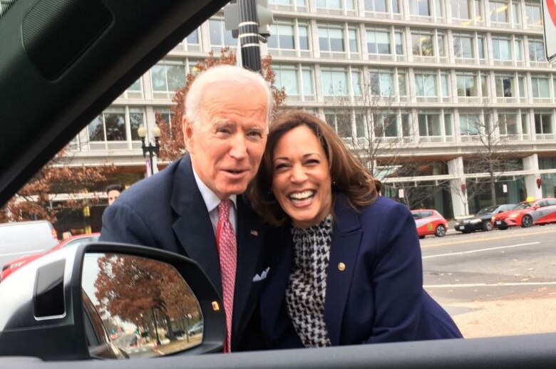 Joe Biden and Kamala Harris posing together and smiling while a photo is taken through a car window