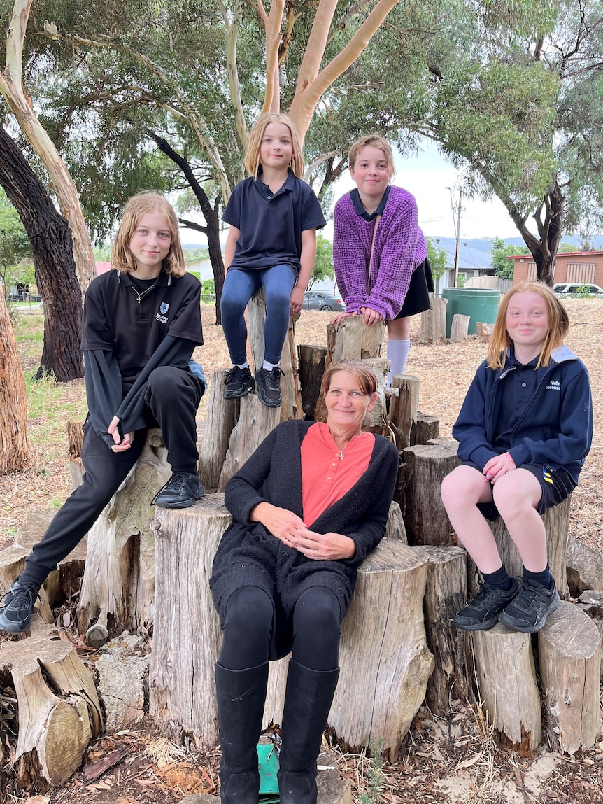 A woman sitting on tree logs with four children around her