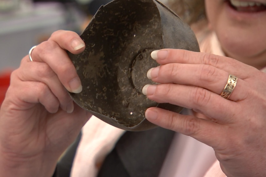 A dirty brown round container is held up by two hands.