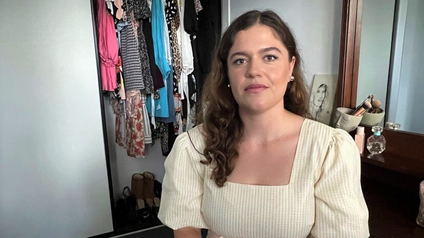 Girl looks at camera in front of clothes cupboard. 