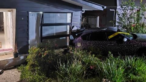 A car rests in the side of a house - which it reversed into.