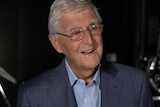 Michael Parkinson wears a checked suit, blue shirt and glasses.