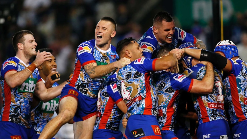 A group of NRL players jump on top of a tryscorer in celebration.
