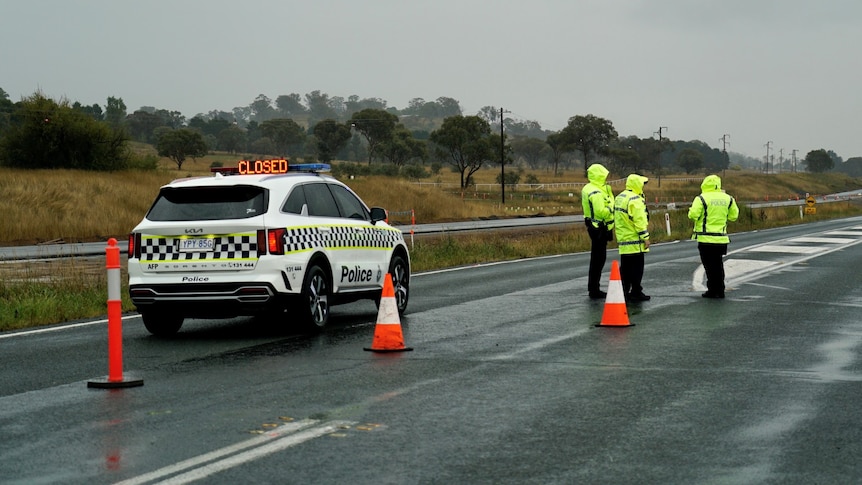 Three police officers in hi-viz clothing stand on a road near a police car.