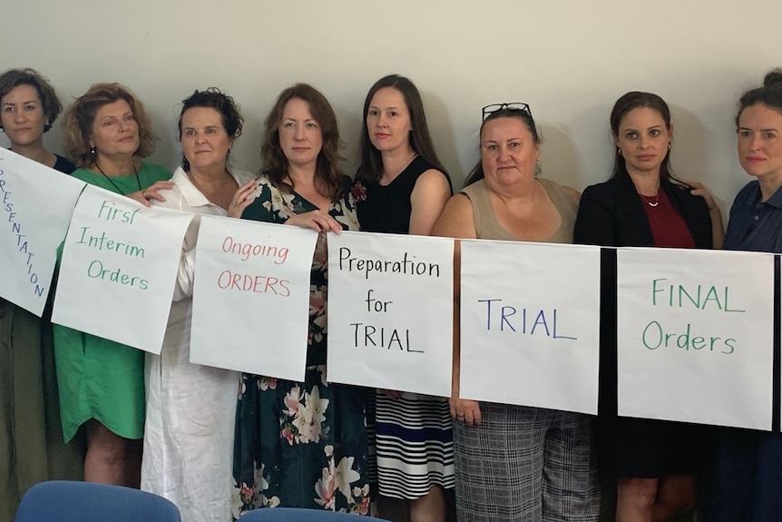 Eight women stand together holding signs about the court system