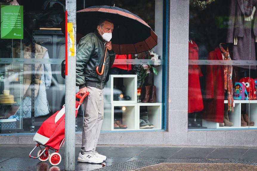A man under an umbrella with a shopping trolley. 