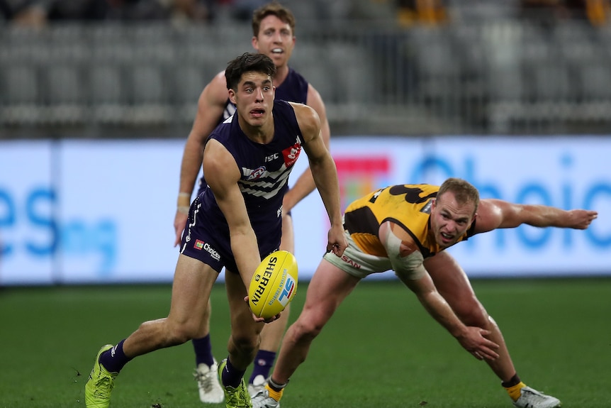 Adam Cerra of the Fremantle Dockers handballs the football after evading a tackle by Hawthorn's Tom Mitchell