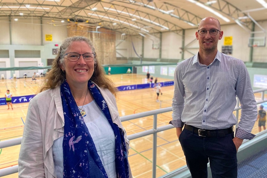 Two Noosa Council staff with people playing badminton on courts in the background.