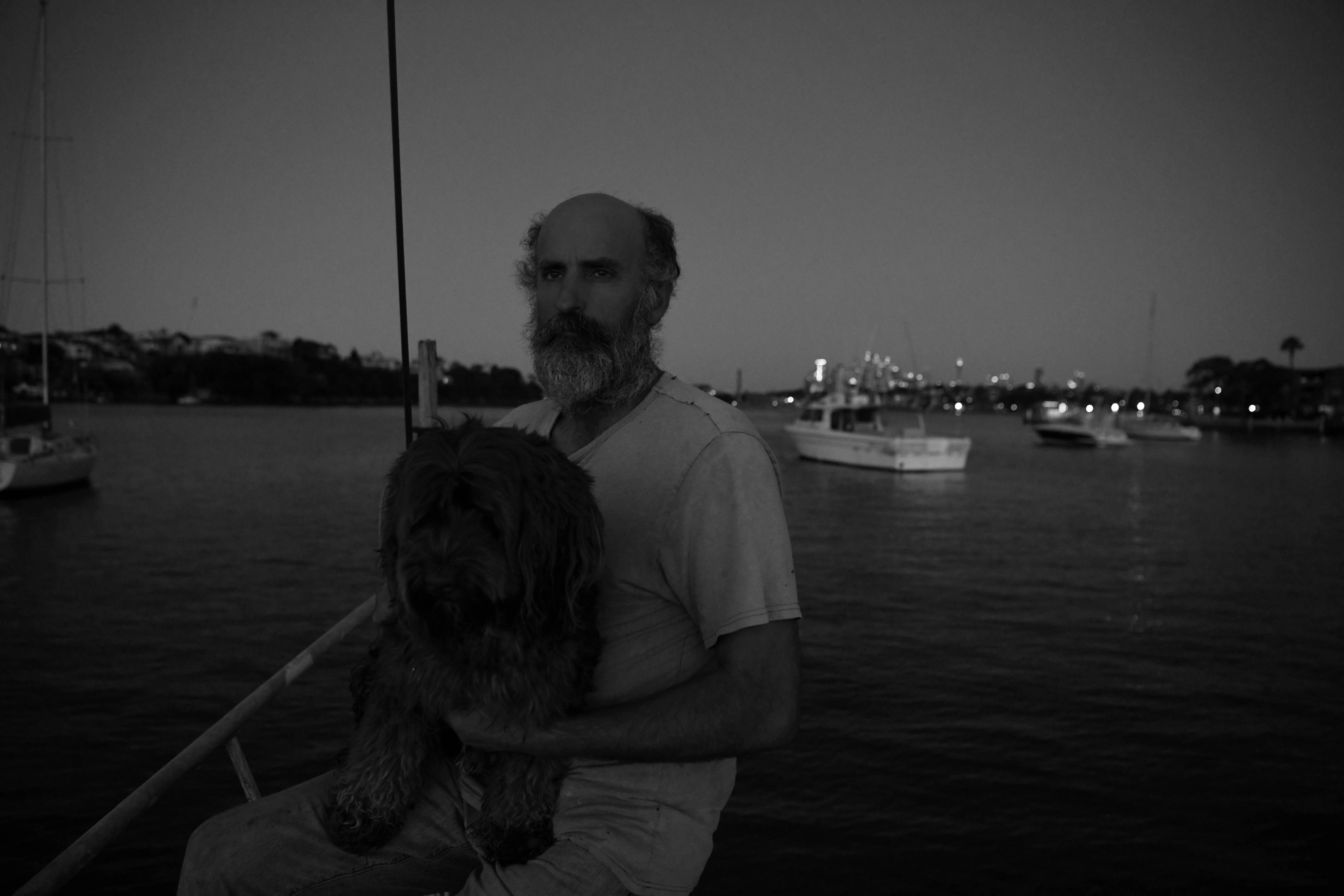 A man carries a shaggy dog in the dark near the water