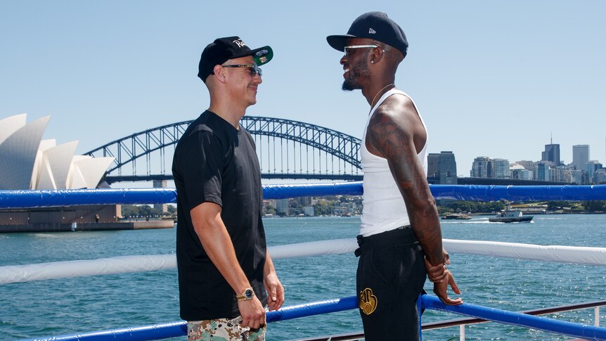 A white man and a black man face off in front of the Sydney Harbour Bridge.