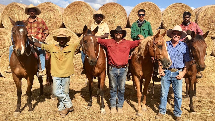 Four indigenous students sitting on horses in front of hay bales.