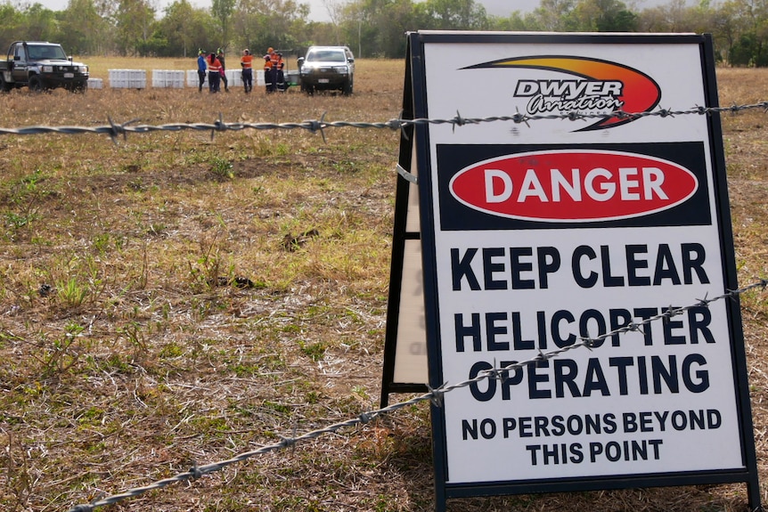 A sign behind a barbwire fence that reads "danger, keep clear, helicopter operating'