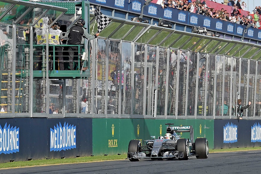 A man in a tower waves the chequered flag as a F1 driver crosses the finish line.