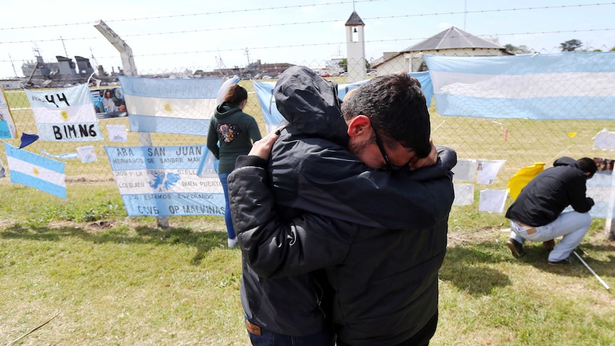 Relatives and friends of Alejandro Damian Tagliapietra hug near banner saying  "Camarades, be strong"